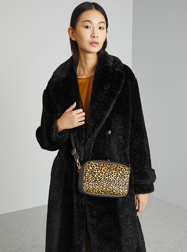 Modella indossa cappotto nero e borsa in fantasia animalier.